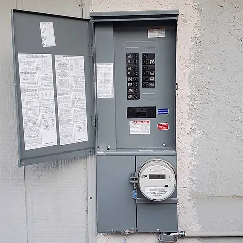 A new grey meter main panel with its door open, mounted on a stucco wall