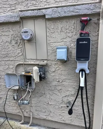 Stucco wall crowded with the old meter, an EV charger, an outlet and junction boxes